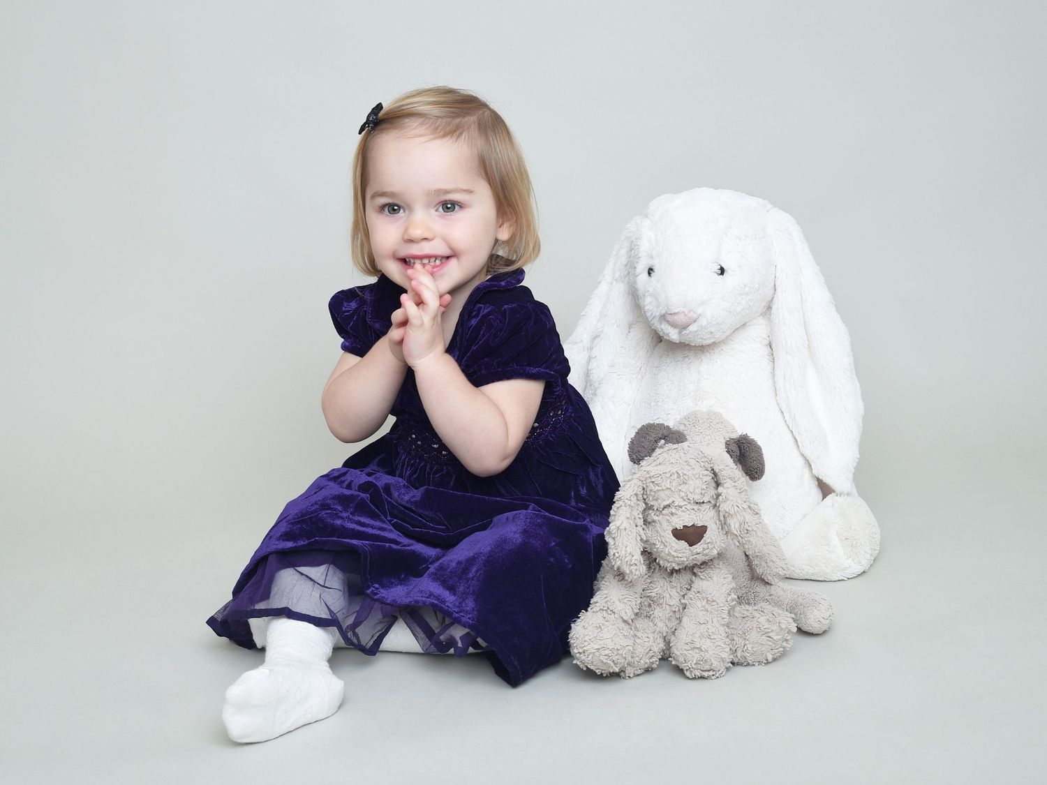 Girl in blue dress smiles happily with teddies on light grey back drop. Family studio photography by Abigail's Studio in High Wycombe