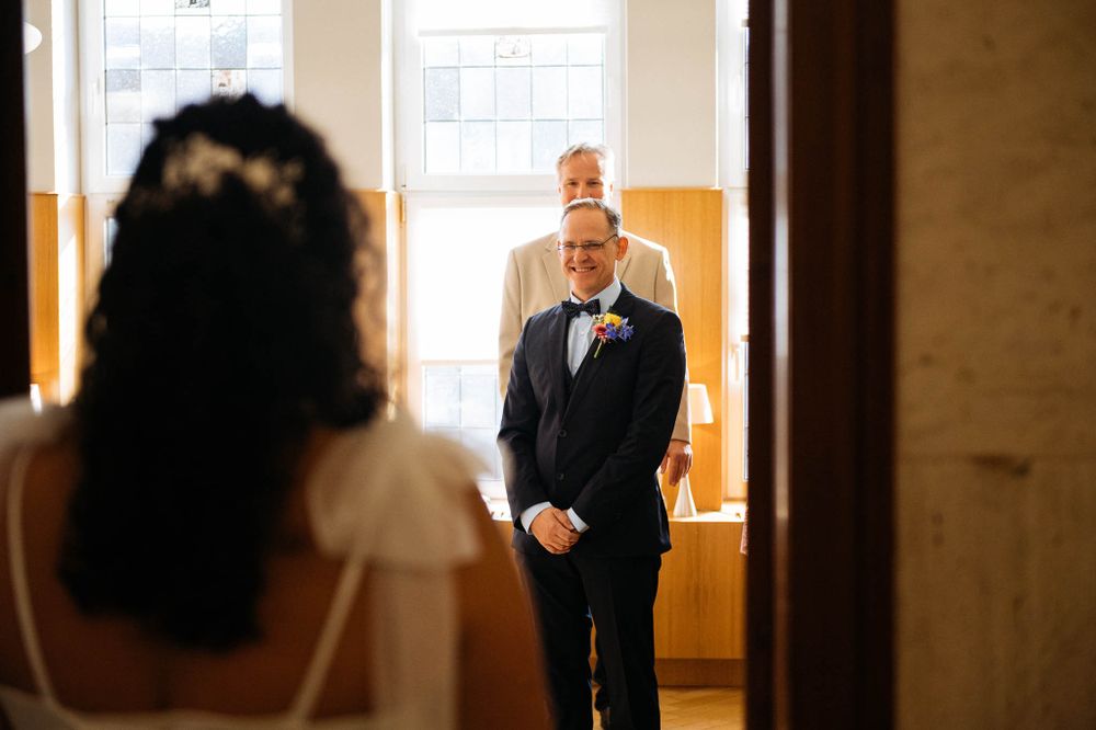 Ein emotionaler ‚First Look‘-Moment zwischen einem Paar an ihrem Hochzeitstag in einem warm beleuchteten Flur.
