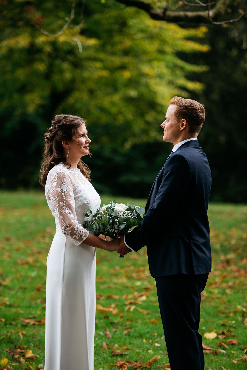 Romantische Outdoor-Hochzeits-Szene mit einem Paar in einem Garten mit Herbstlaub und einem Brautstrauß.