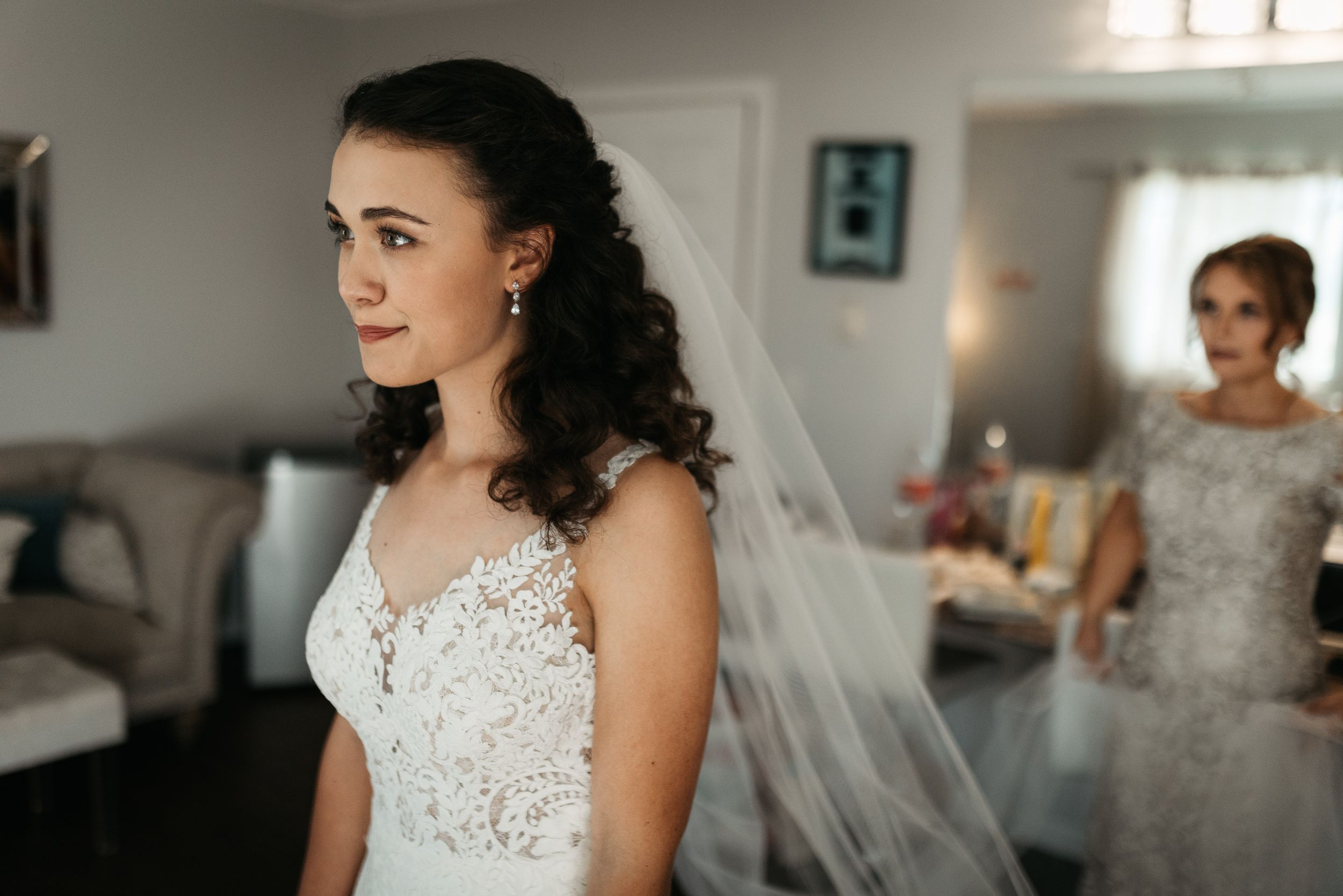 A bride in a delicate white lace wedding gown stands in profile while wearing a long flowing veil.