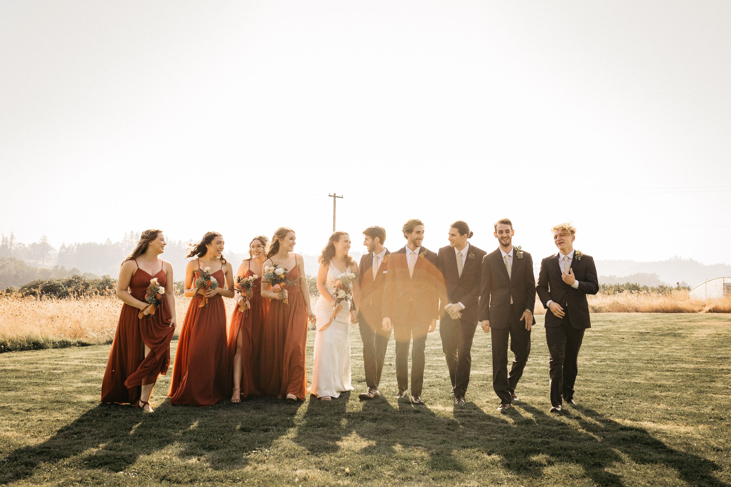 Wedding party poses together at sunset in an open field casting long shadows against golden light.