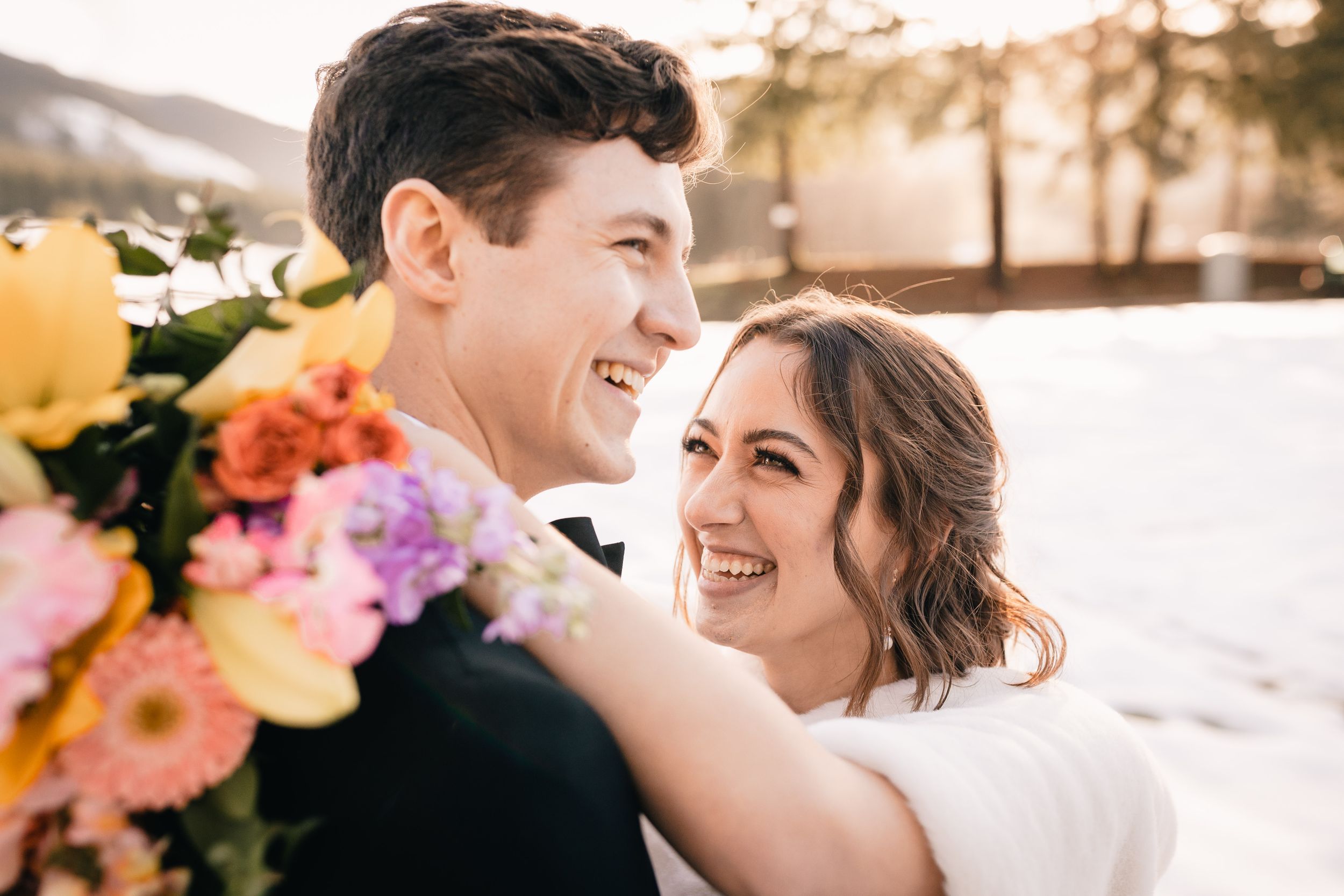A happy newlywed couple embraces outdoors in winter with colorful flowers in view during their wedding.