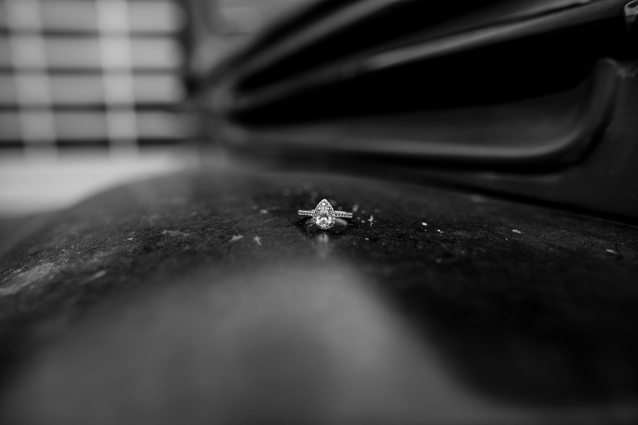 Close-up macro shot of a diamond engagement ring on dark reflective surface.