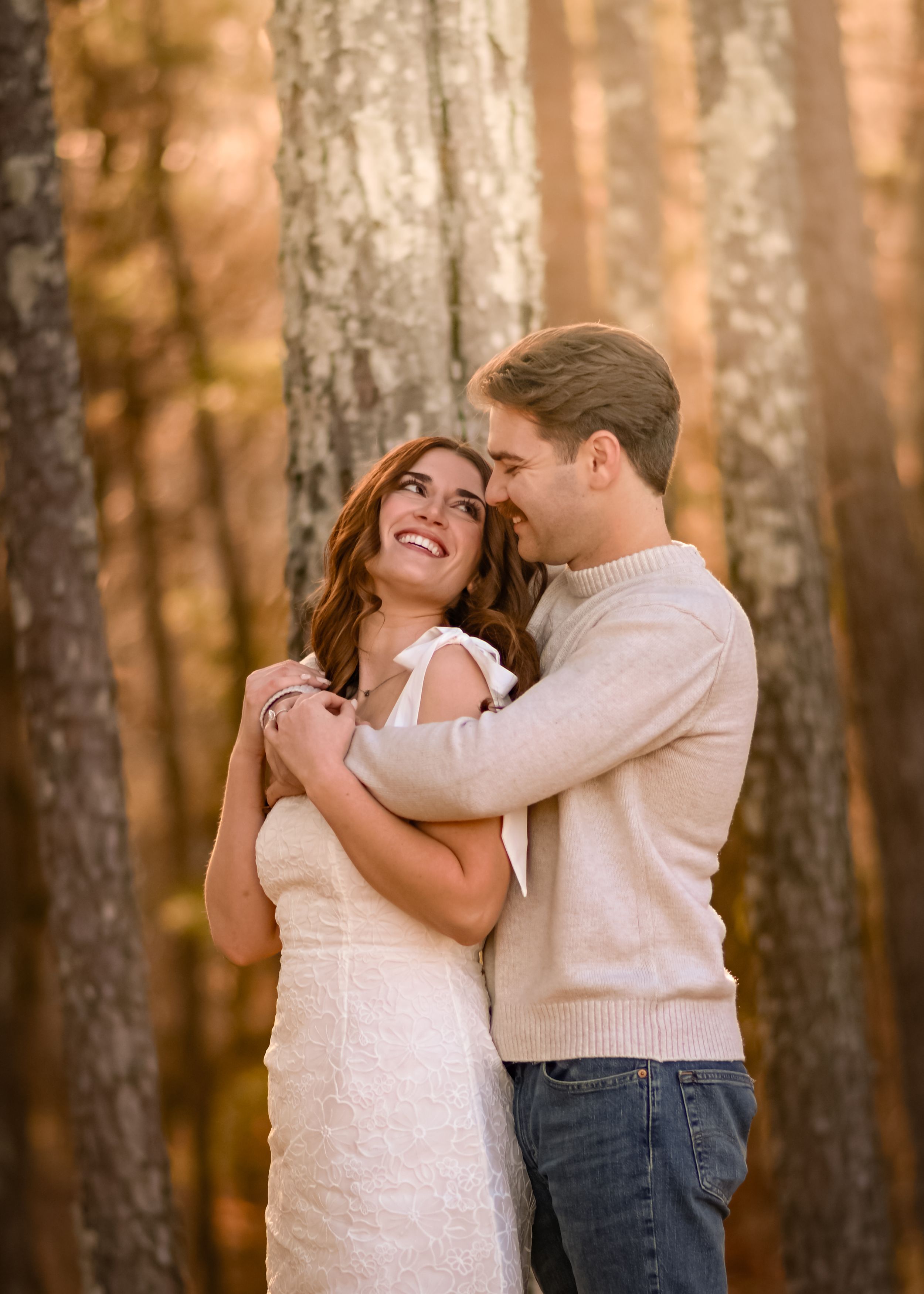 A couple embraces in a sunlit forest setting during golden hour.