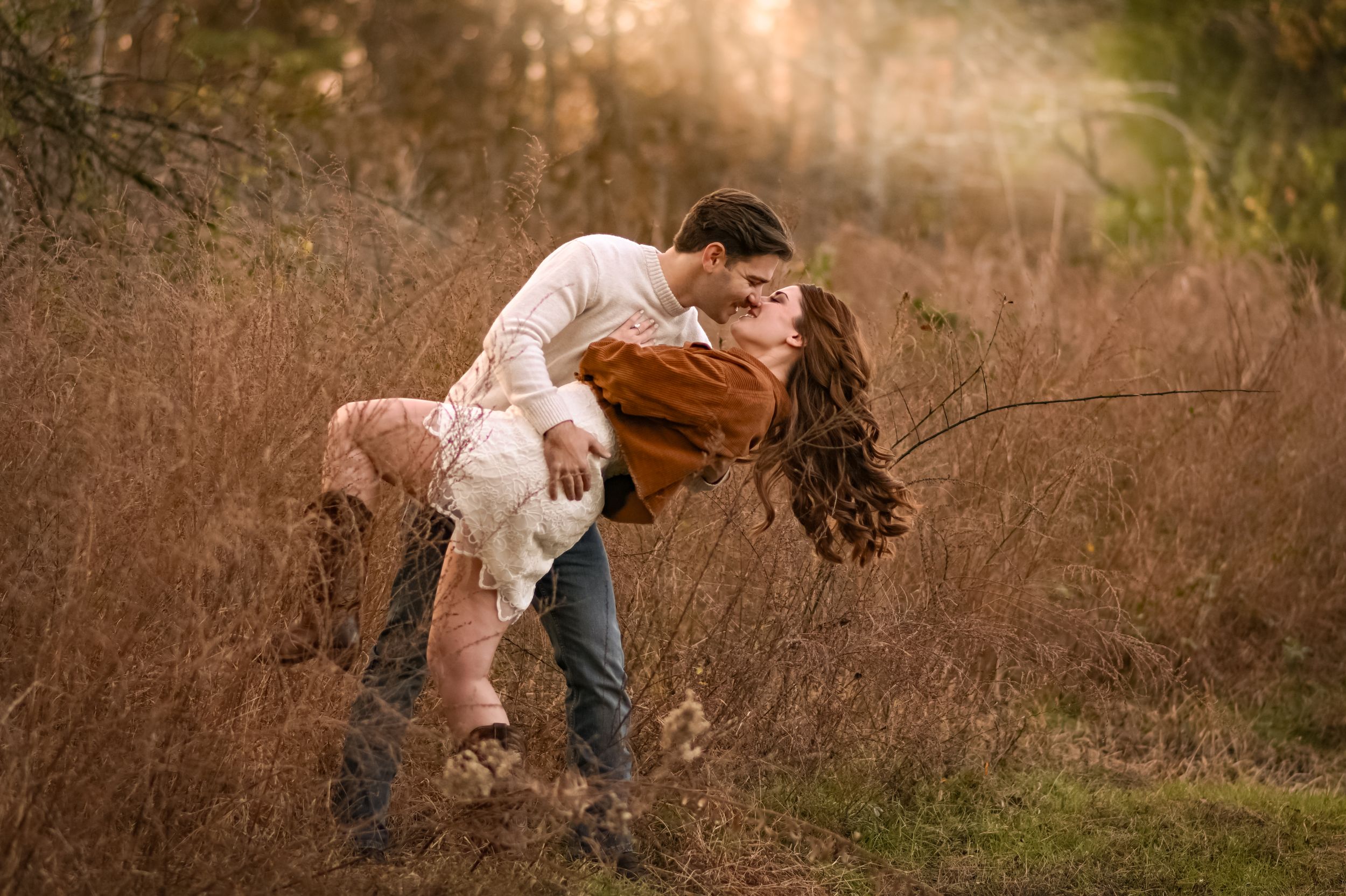 A couple playfully interacts in a wooded area during sunset.