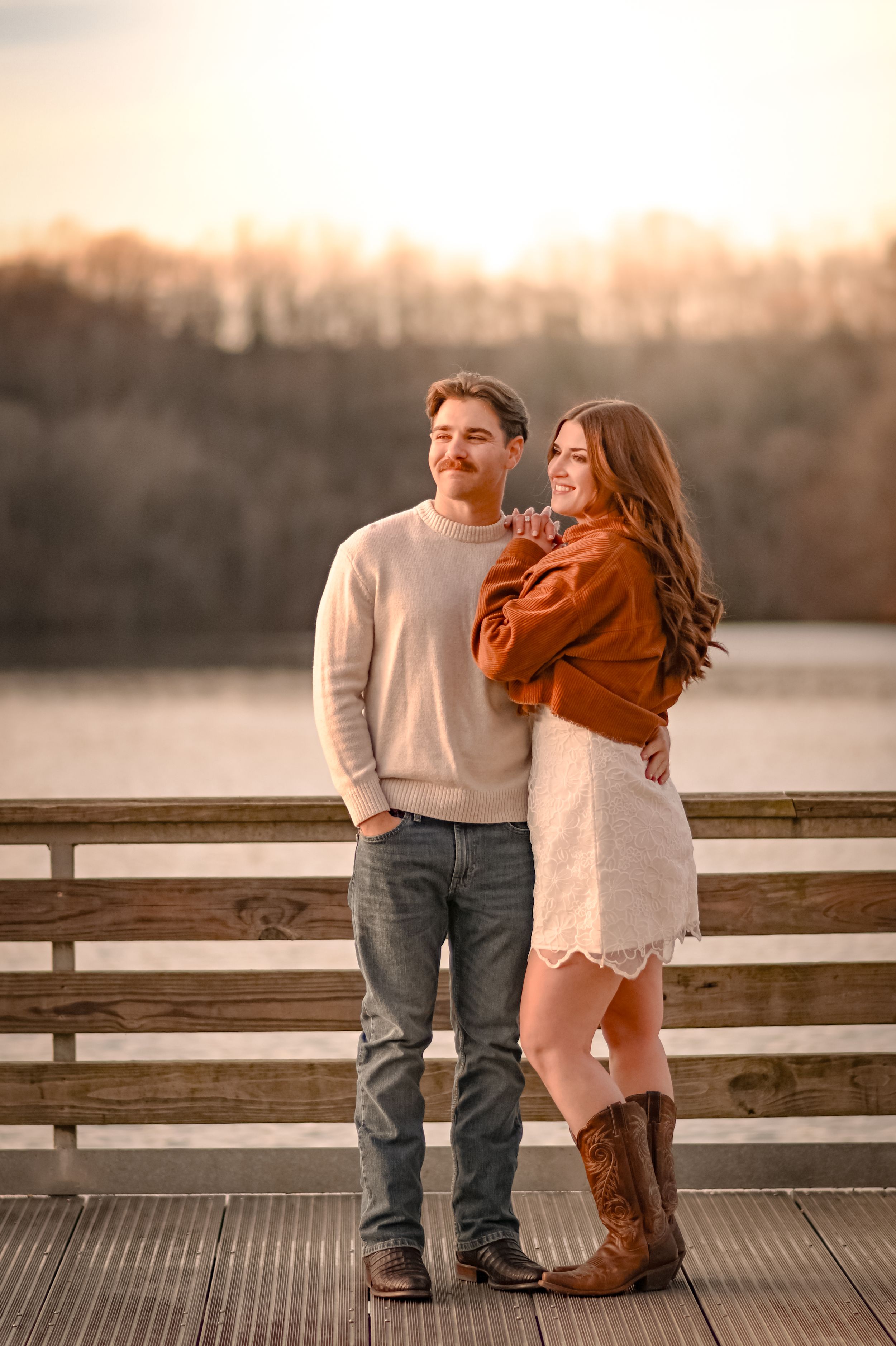 A couple shares a tender moment on a wooden dock at sunset.