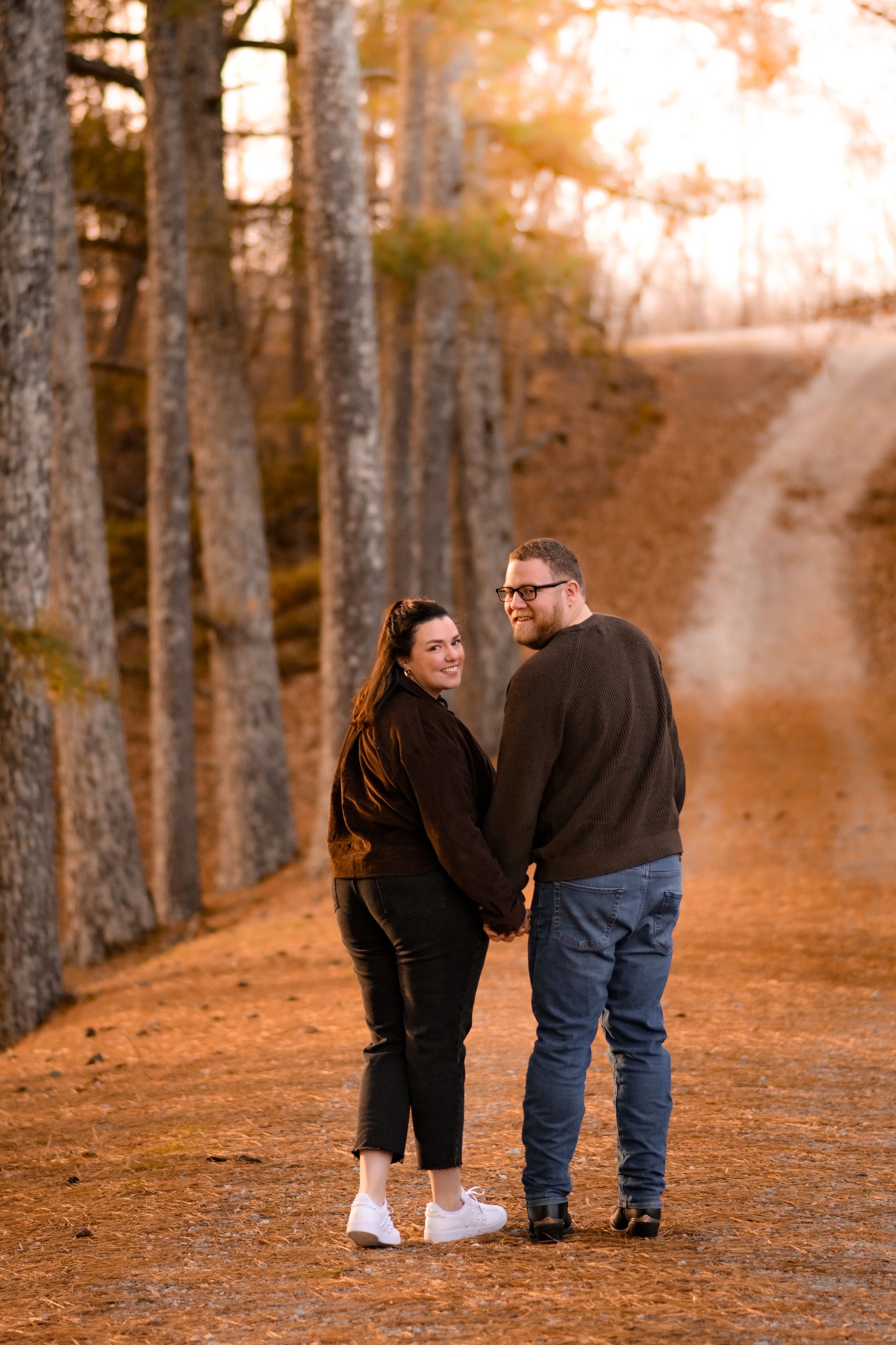 A couple strolls together through a forest path during golden hour.