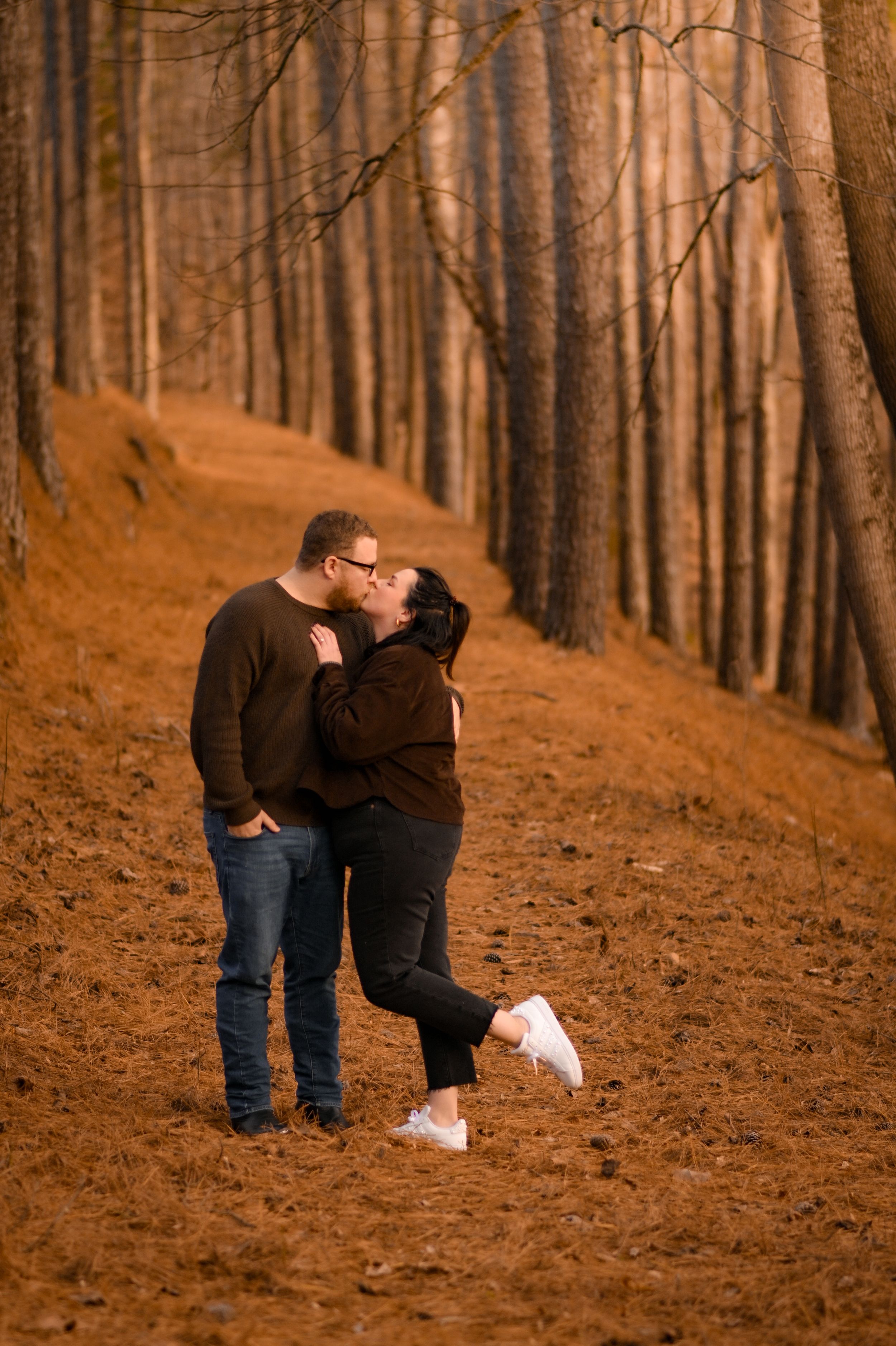 A couple walks together on a sloped forest trail during sunset.