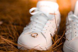 A white sneaker with an engagement ring balanced on top against a brown grassy background.