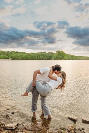 Playful couple enjoying time together by a scenic lake with dramatic cloudy sky.
