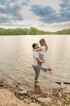 Couple having fun and playing near the water's edge at a lake during sunset.