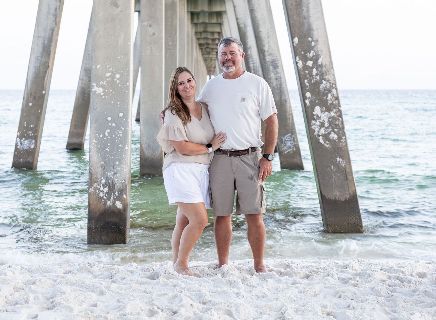 husband and wife on beach with pier