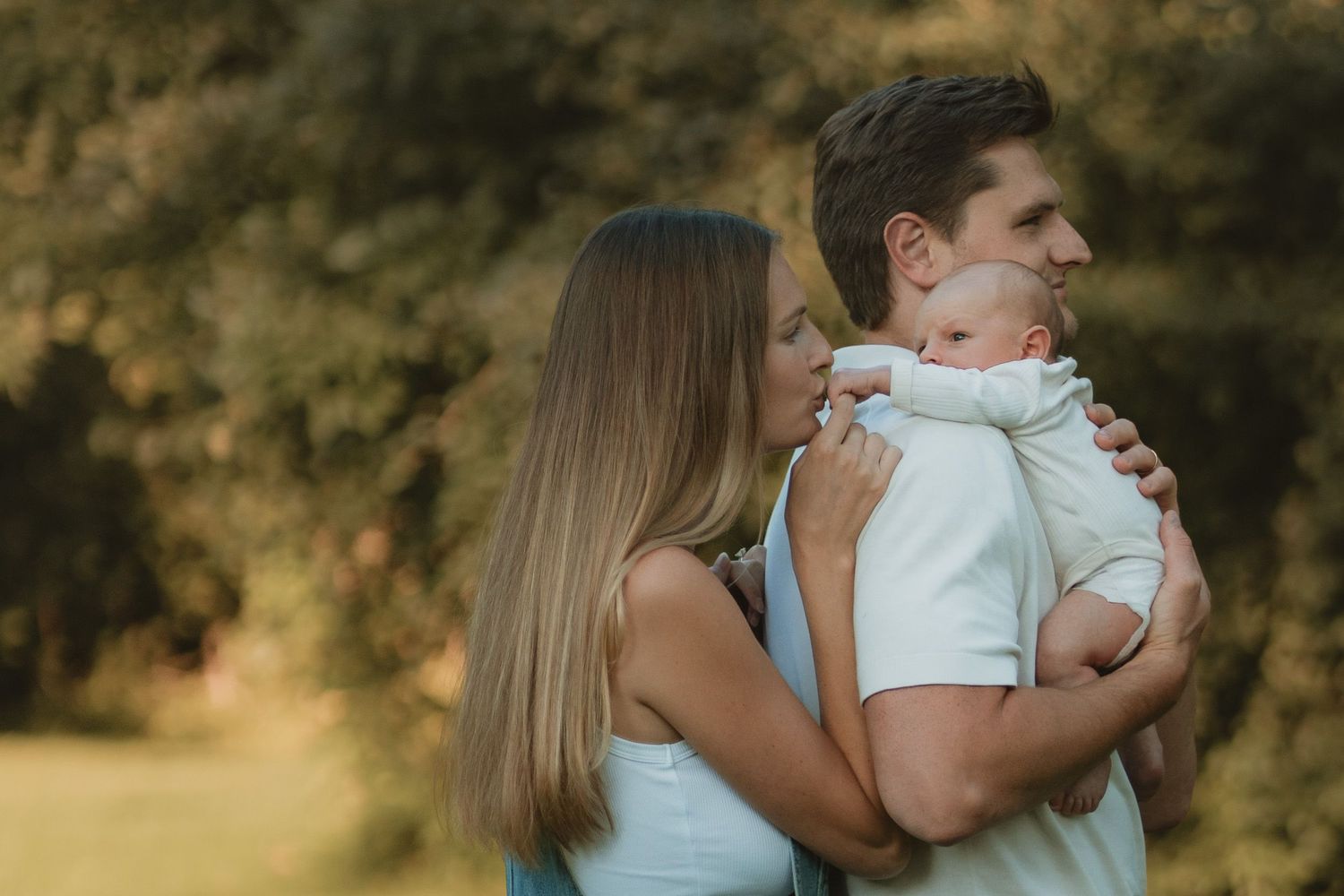 A young couple embraces outdoors while holding a newborn baby in Lake Forest