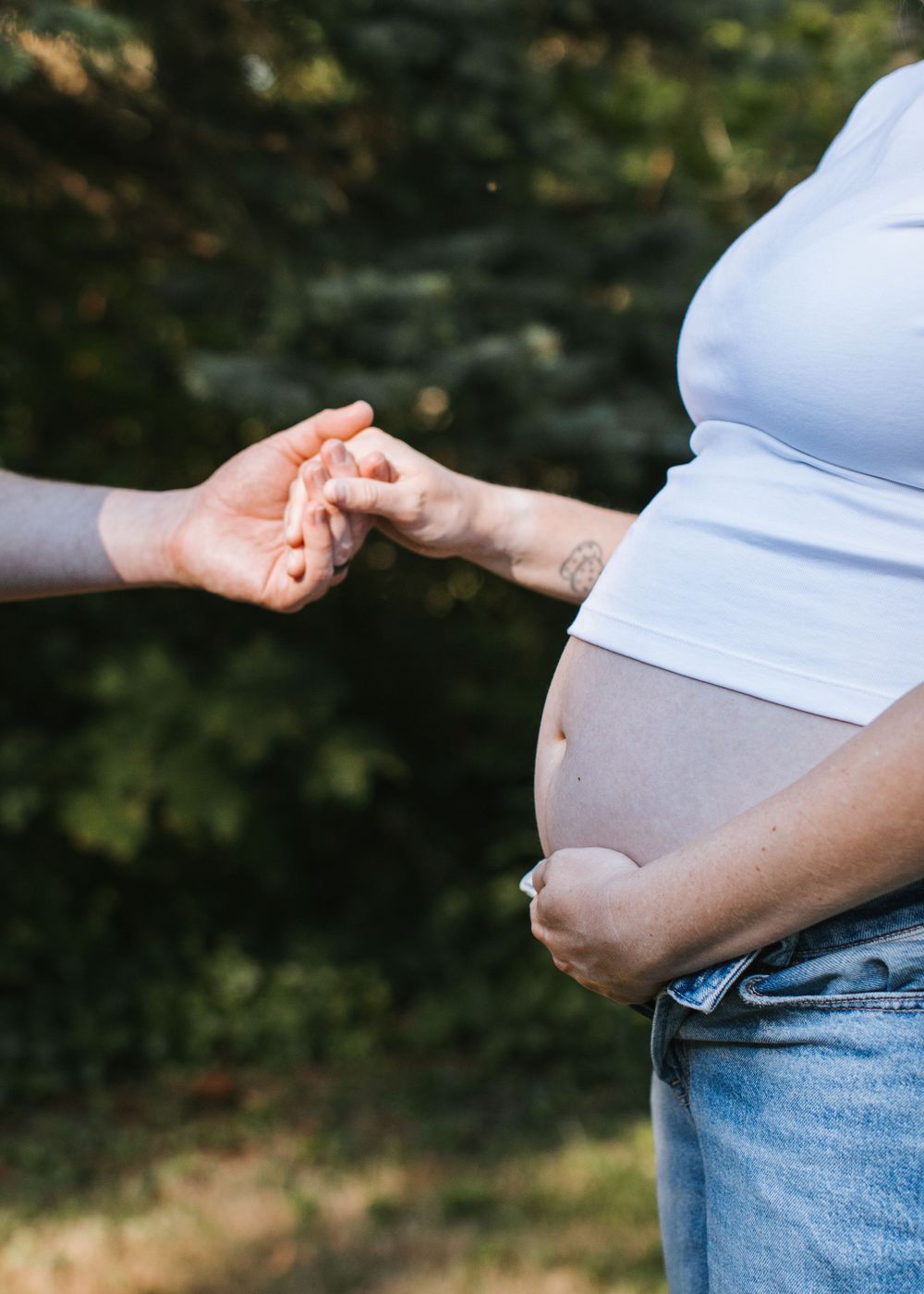Sweet handholding moment with pregnant belly during outdoor lifestyle maternity session in Flint, Michigan