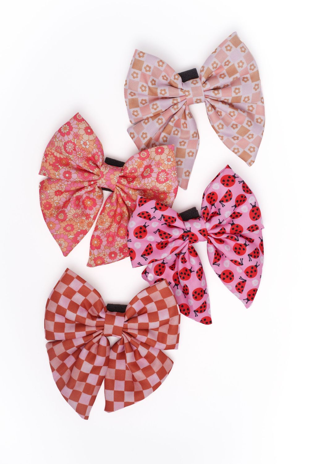 Four decorative fabric hair bows in pink patterns including floral, ladybug, and checkered designs on white background.