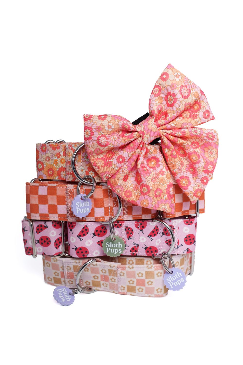 Stack of pink and orange floral dog collars with a large bow topper, featuring ladybug and checkered patterns by Sloth Pups.