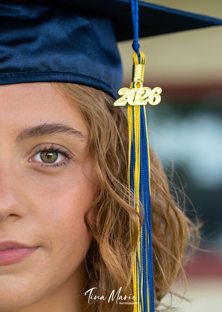 Close-up portrait of a young woman wearing a navy blue graduation cap with a 2026 tassel in blue and gold.