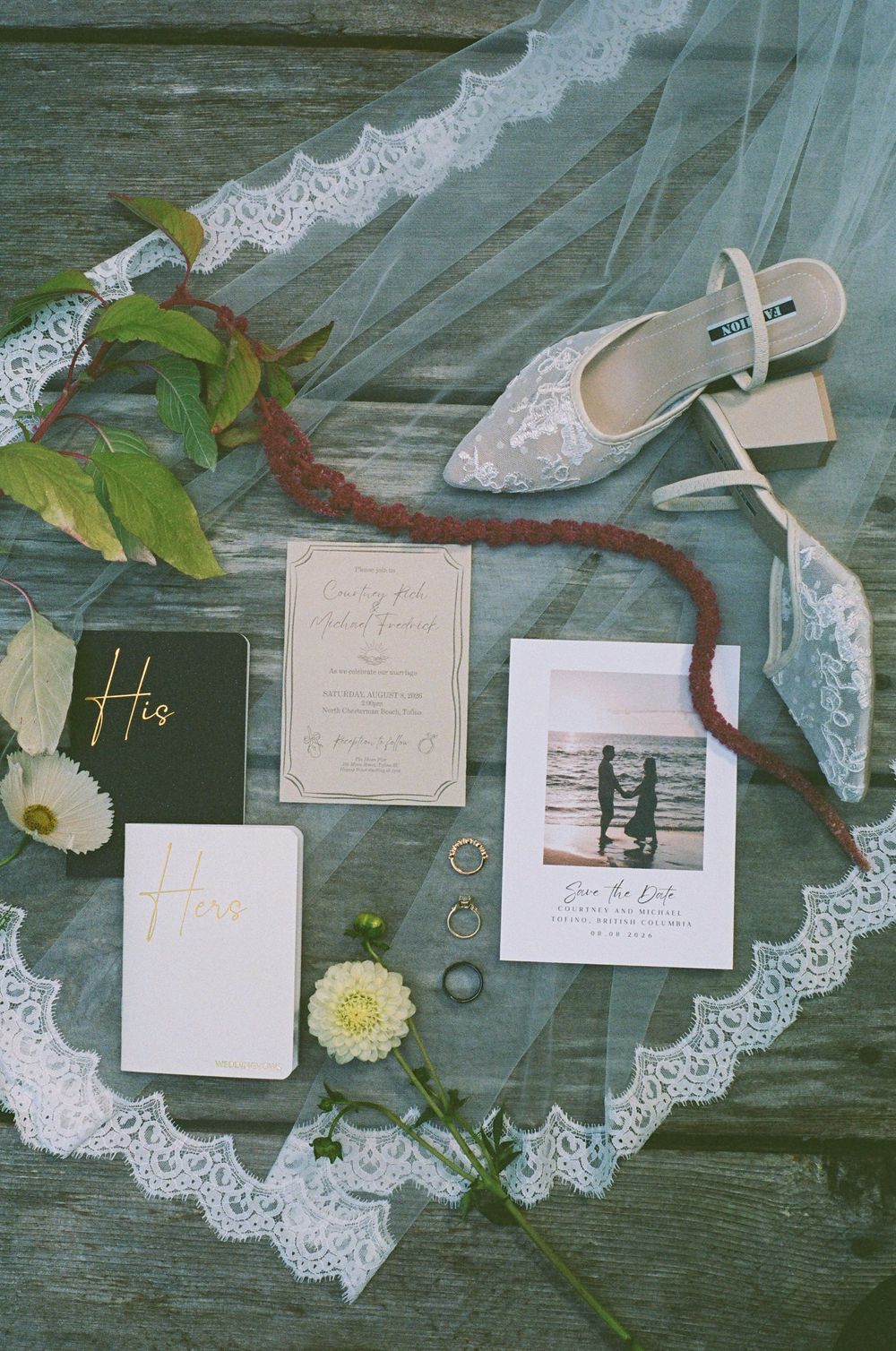 Wedding flat lay with lace veil, bridal shoes, invitations, rings, and save the date card.