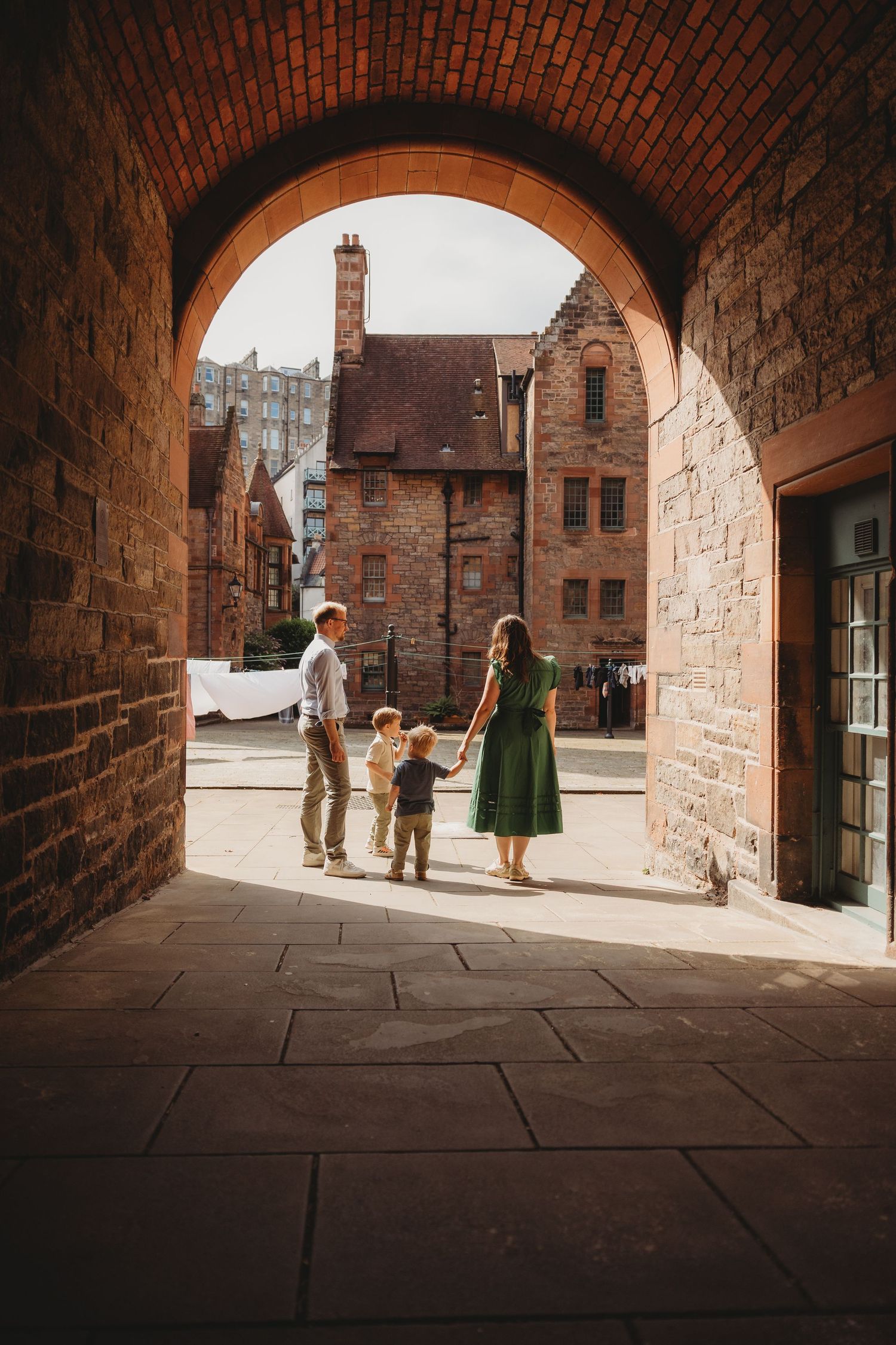 Family of four standing under a brick archway in a historic cobblestone courtyard with old stone buildings.