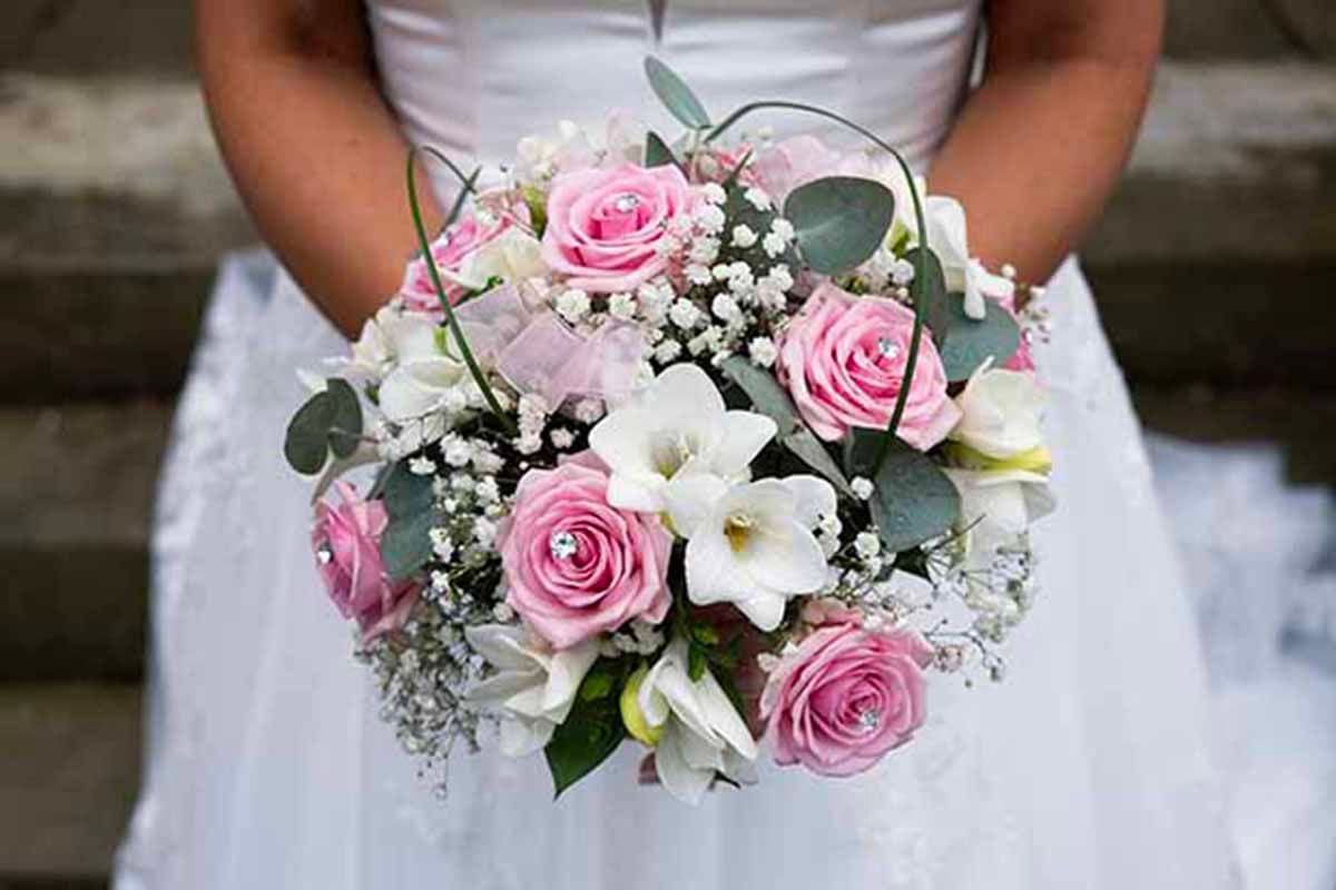 Bride holding a round wedding bouquet with pink roses, white lilies, and baby's breath accents.