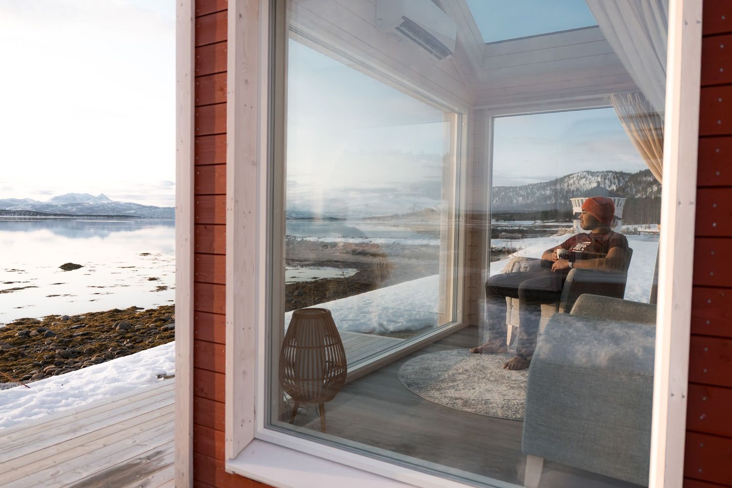 hotel tout en baie vitrée au bord du fjord avec un homme qui regarde le paysage à senja, norwegian wild
