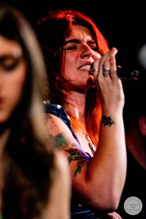 Tattooed redhead female vocalist singing passionately into microphone during live concert performance.
