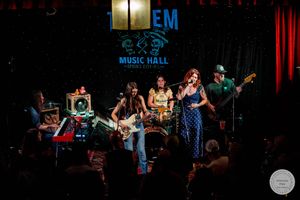 Live band performs on stage at 10EM Music Hall, featuring female musicians with guitars under colorful stage lighting.