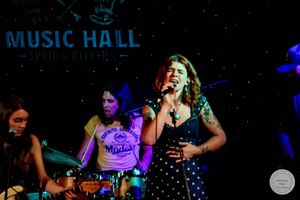 Female singer performs at Music Hall Spring Street with band, wearing polka dot dress under colorful stage lights.