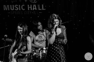 Black and white photo of three women performing at a Music Hall, one singing into a microphone.