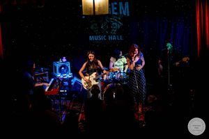 Band performing live on stage at The Gem Music Hall, featuring guitarist and vocalist under colorful lights.