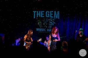 Rock band performs on stage under blue lights at The Gem Music Hall.