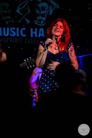 Redhead female vocalist performing energetically on stage at Music Hall Spring City in blue polka dot dress.