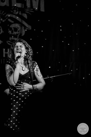 Female vocalist sings passionately on stage in black and white concert photo.