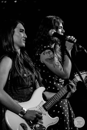 Two female musicians play guitar and sing on stage in black and white photo.