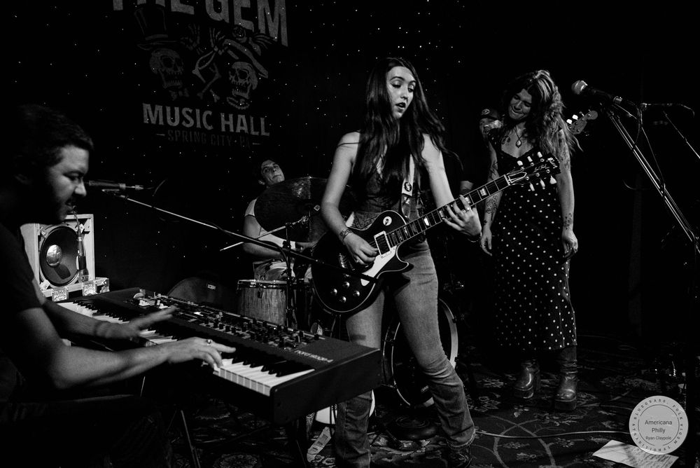 Black and white photo of a female guitarist performing on stage at The Gem Music Hall with her band.