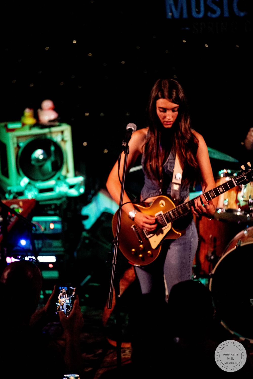 Young woman playing a Les Paul guitar on stage at Music Hall Spring City during a live performance.
