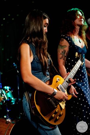 Female guitarist plays gold Les Paul guitar on stage at live concert.
