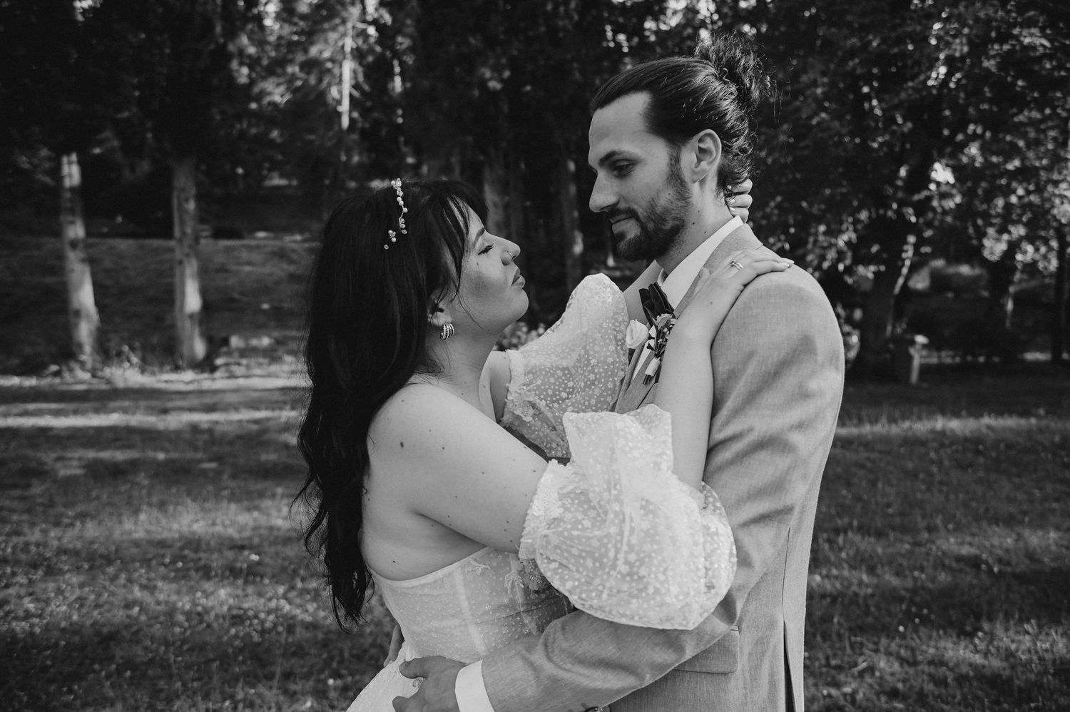 Black and white wedding photo of bride and groom gazing at each other outdoors among trees.