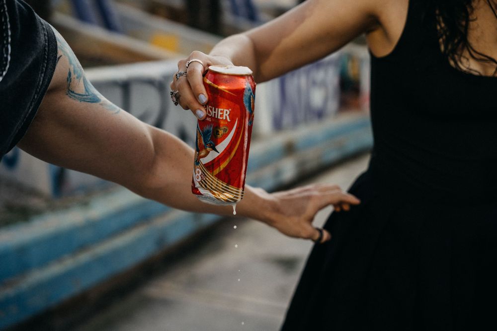 Two people sharing a red beer can outdoors, with liquid dripping, showcasing a casual social moment.