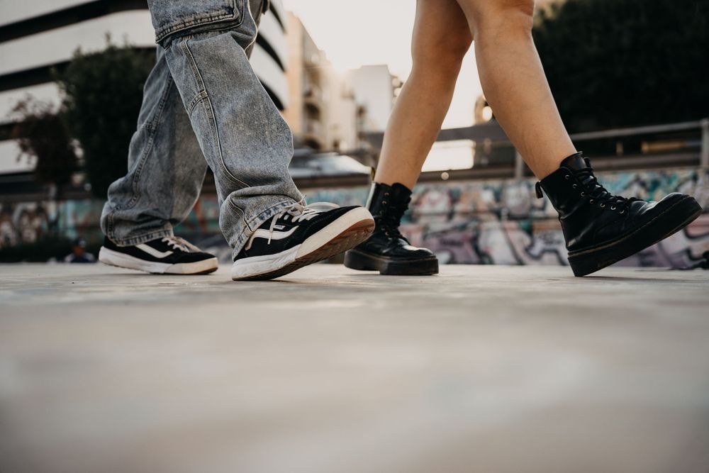 Close-up of two people walking in stylish sneakers and boots on a graffiti-decorated urban pavement.