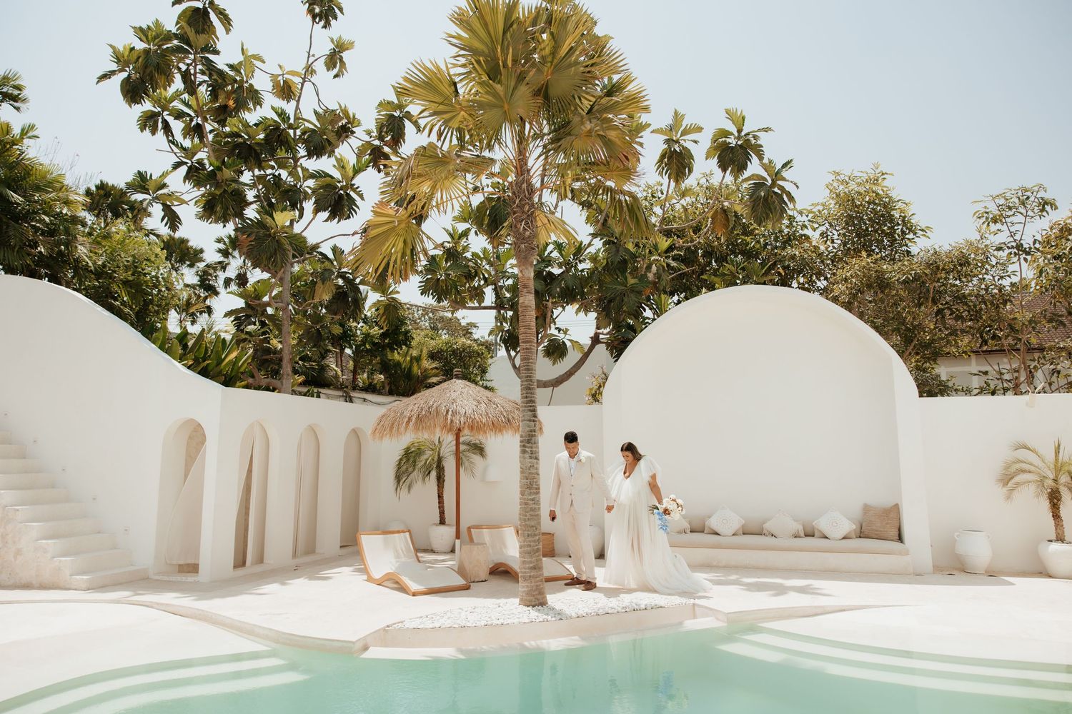 Modern white Mediterranean-style venue with pool and palm trees for wedding ceremony.