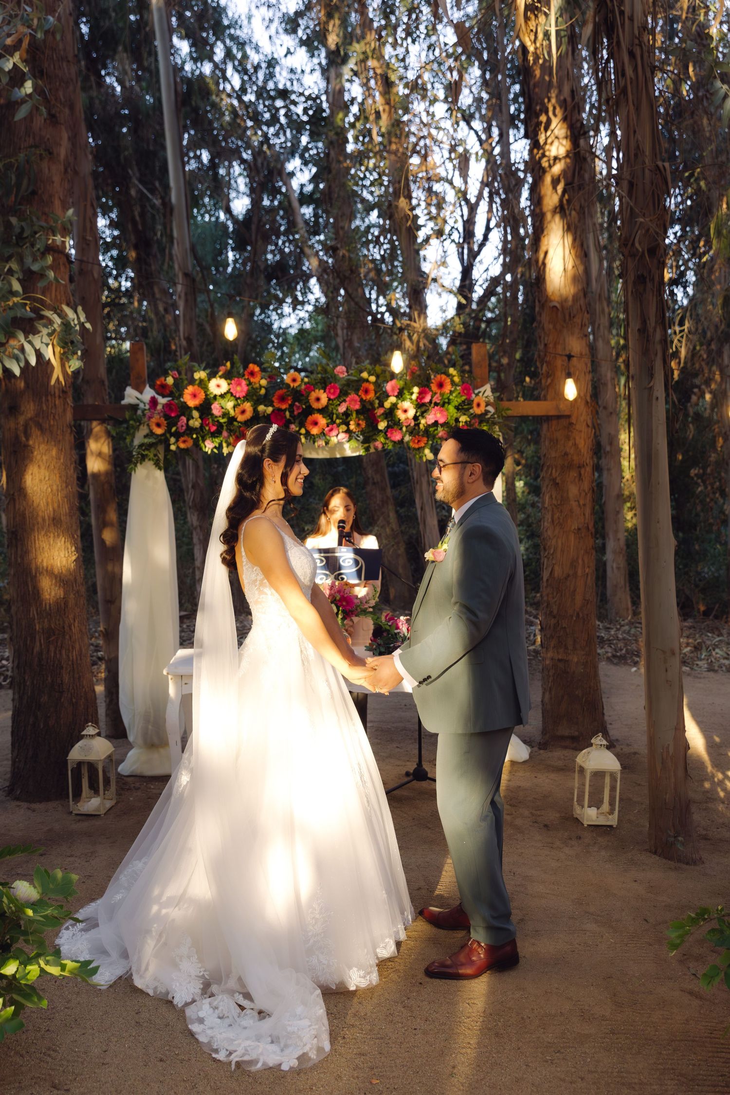 Bride and groom holding hands at altar beneath floral arch in forest wedding.