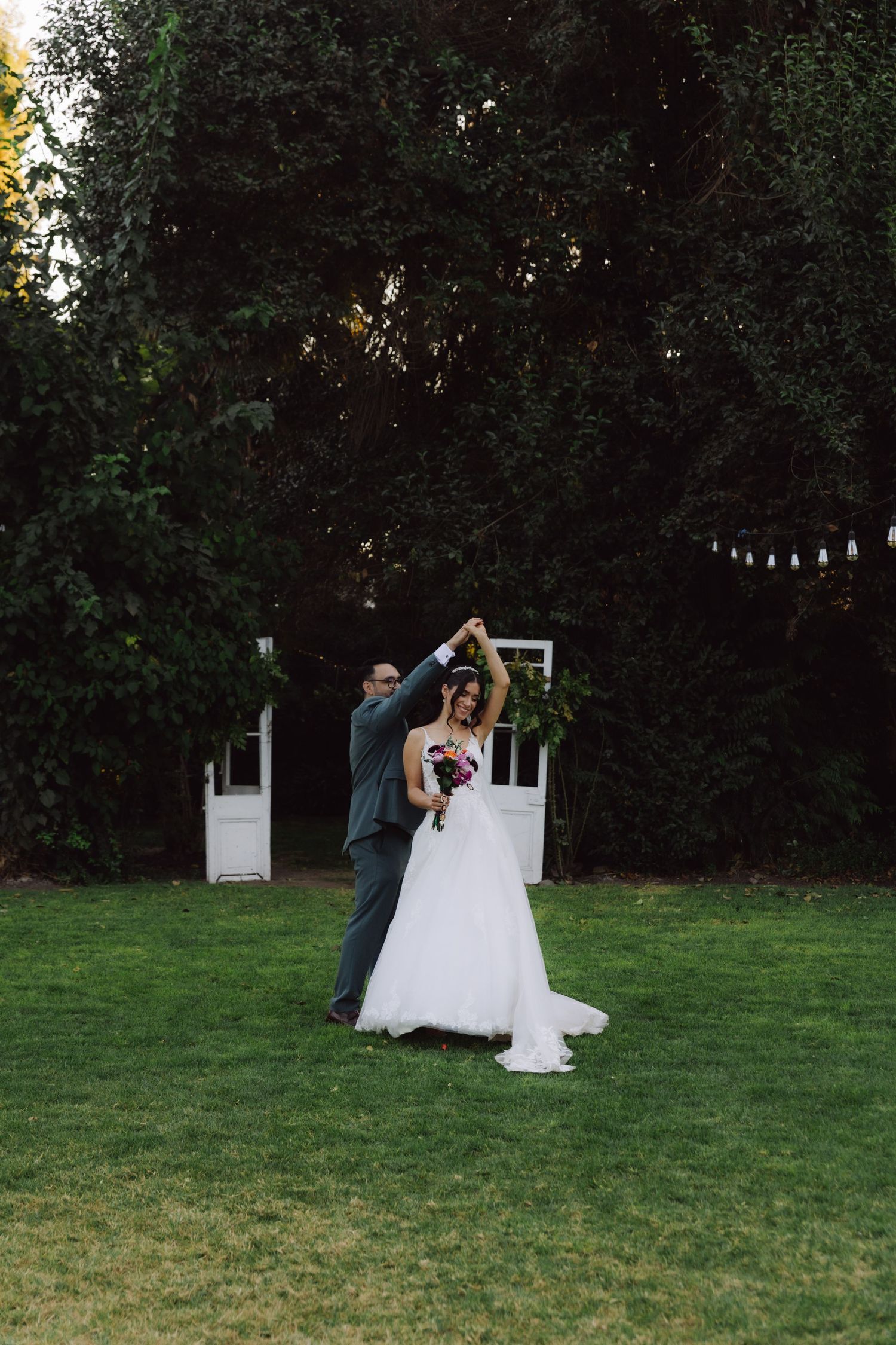 Bride and groom dancing together on green lawn with groom spinning bride at outdoor wedding.