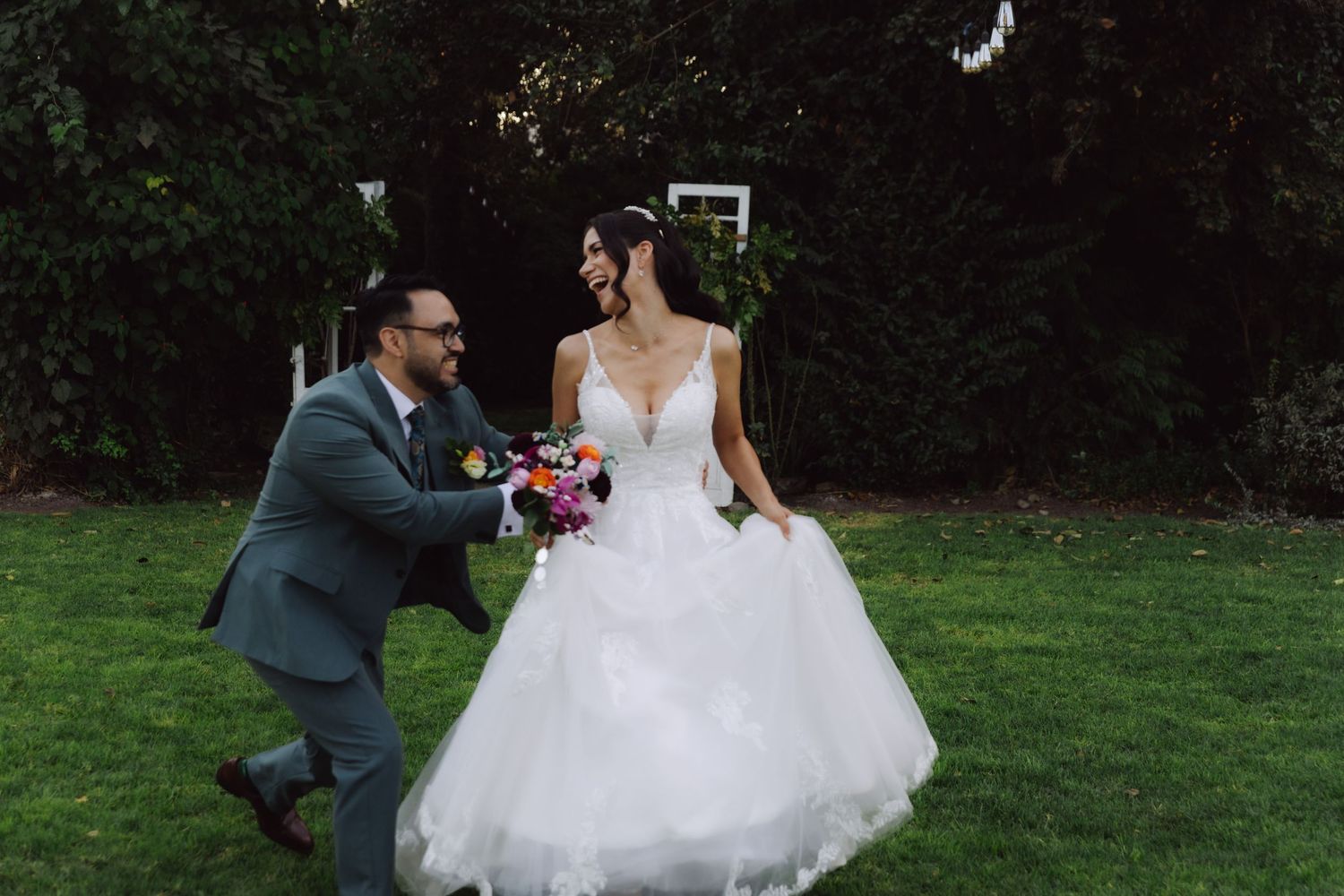 Bride and groom walking hand in hand on lush green lawn during outdoor wedding photo session.