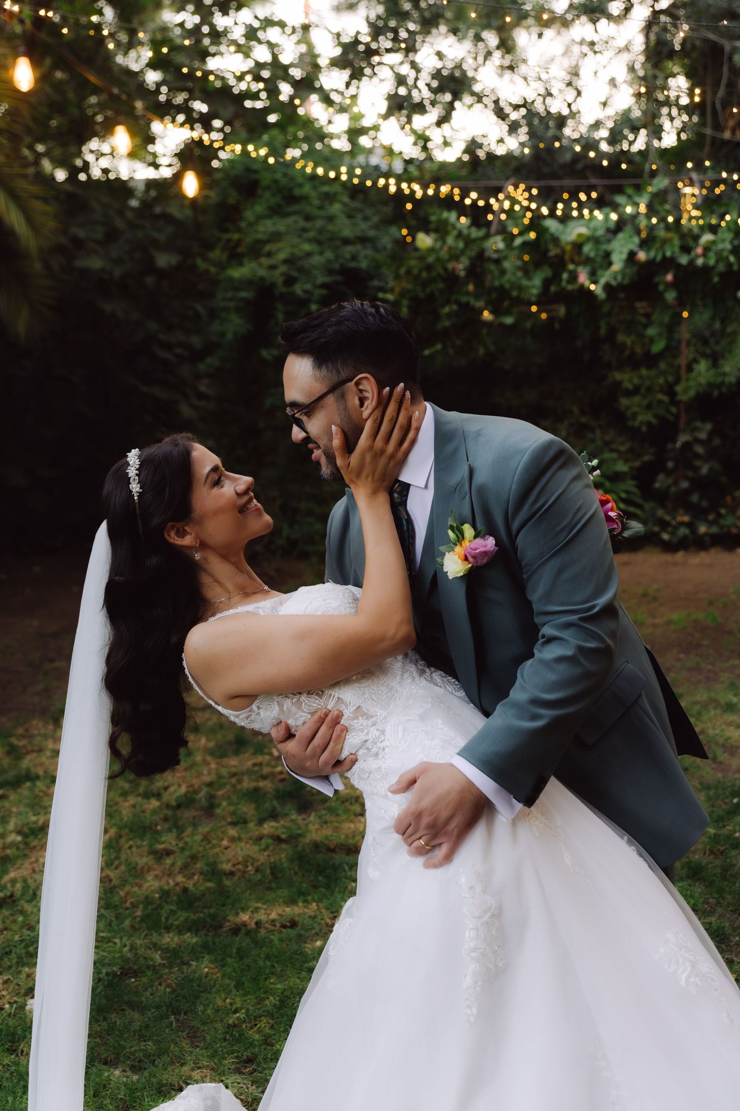 Bride and groom sharing a romantic moment under string lights in a lush garden wedding setting.