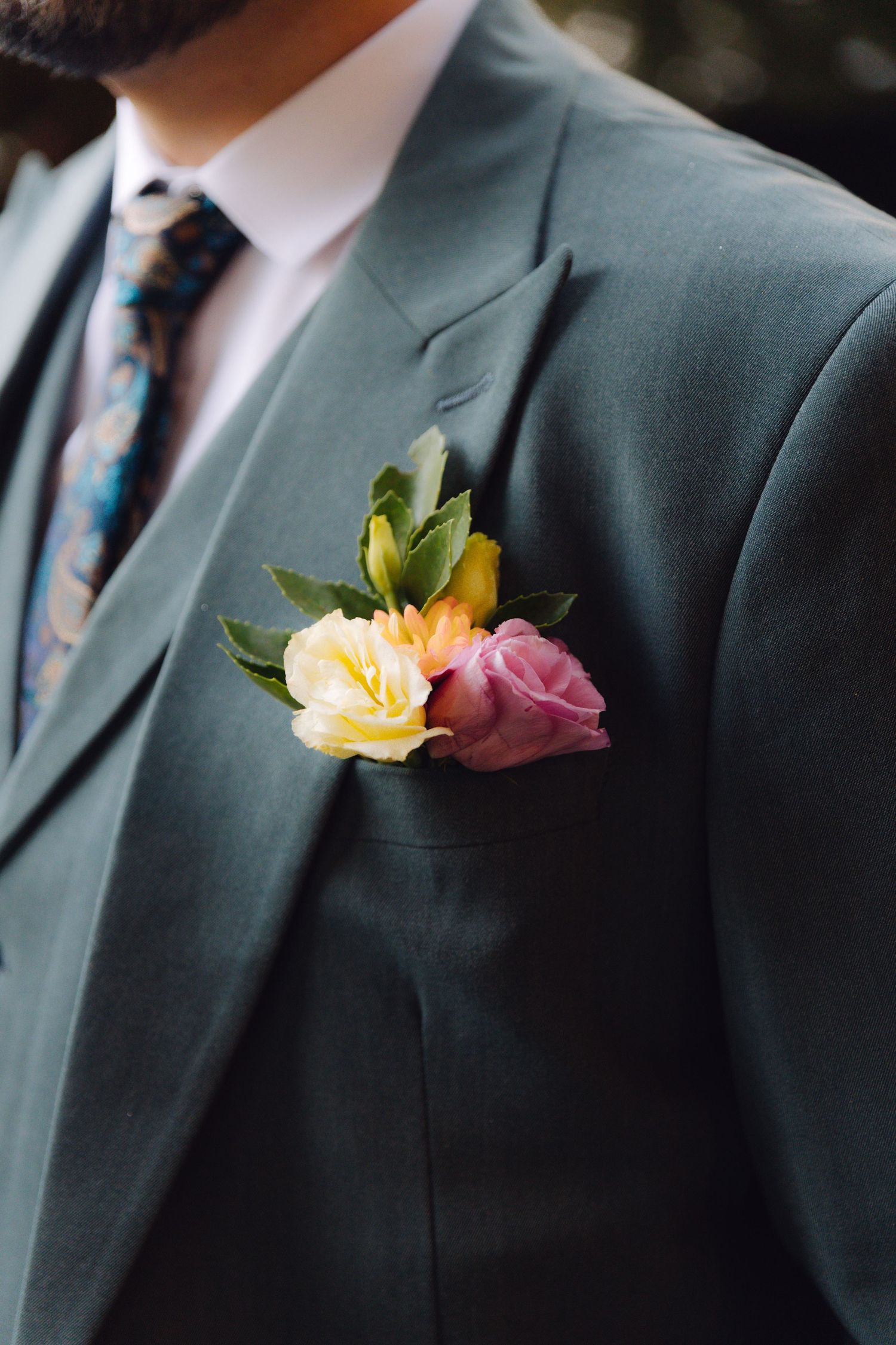 Close-up of a groom's teal suit jacket featuring a colorful pink and yellow floral boutonniere.