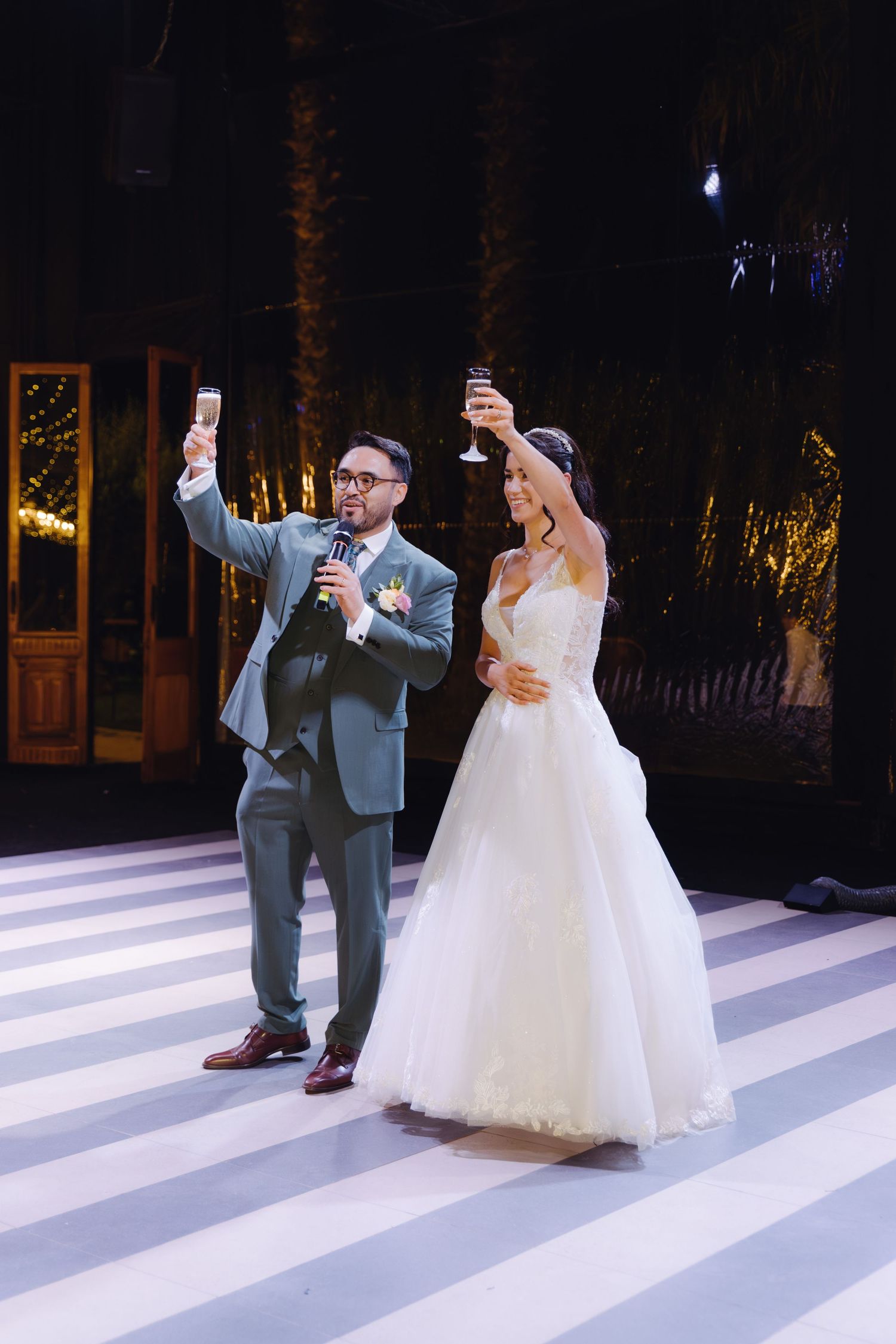 Bride and groom raising champagne glasses in a toast on a striped dance floor at their wedding reception.