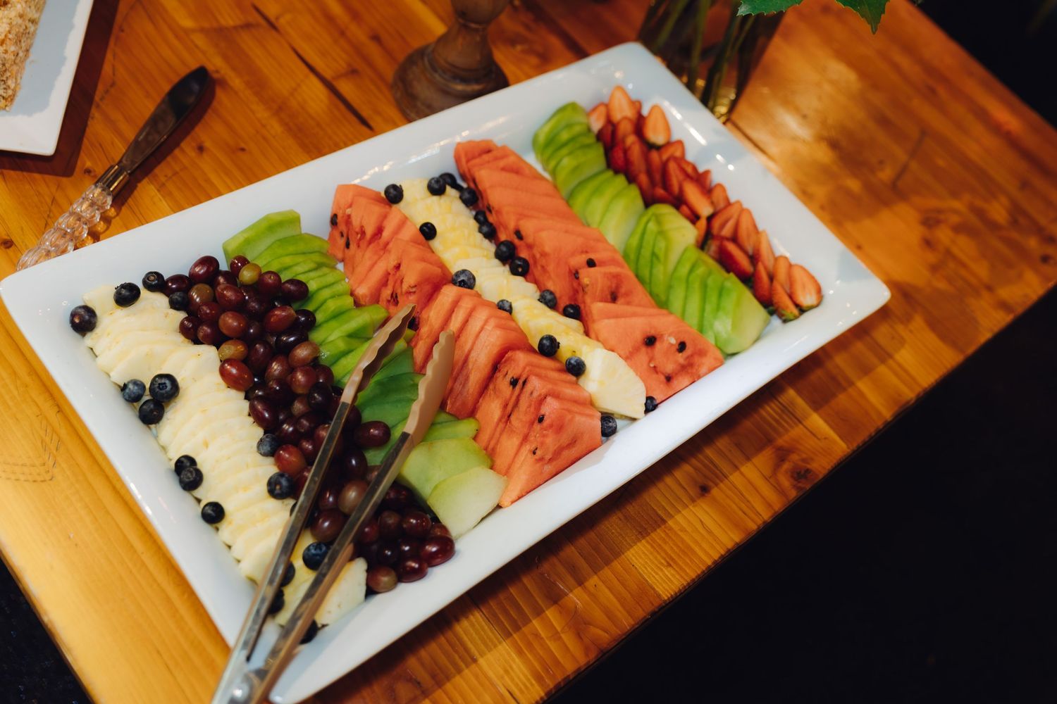 Elegant wedding fruit platter with watermelon, cantaloupe, grapes, and avocado arranged on a white rectangular tray.