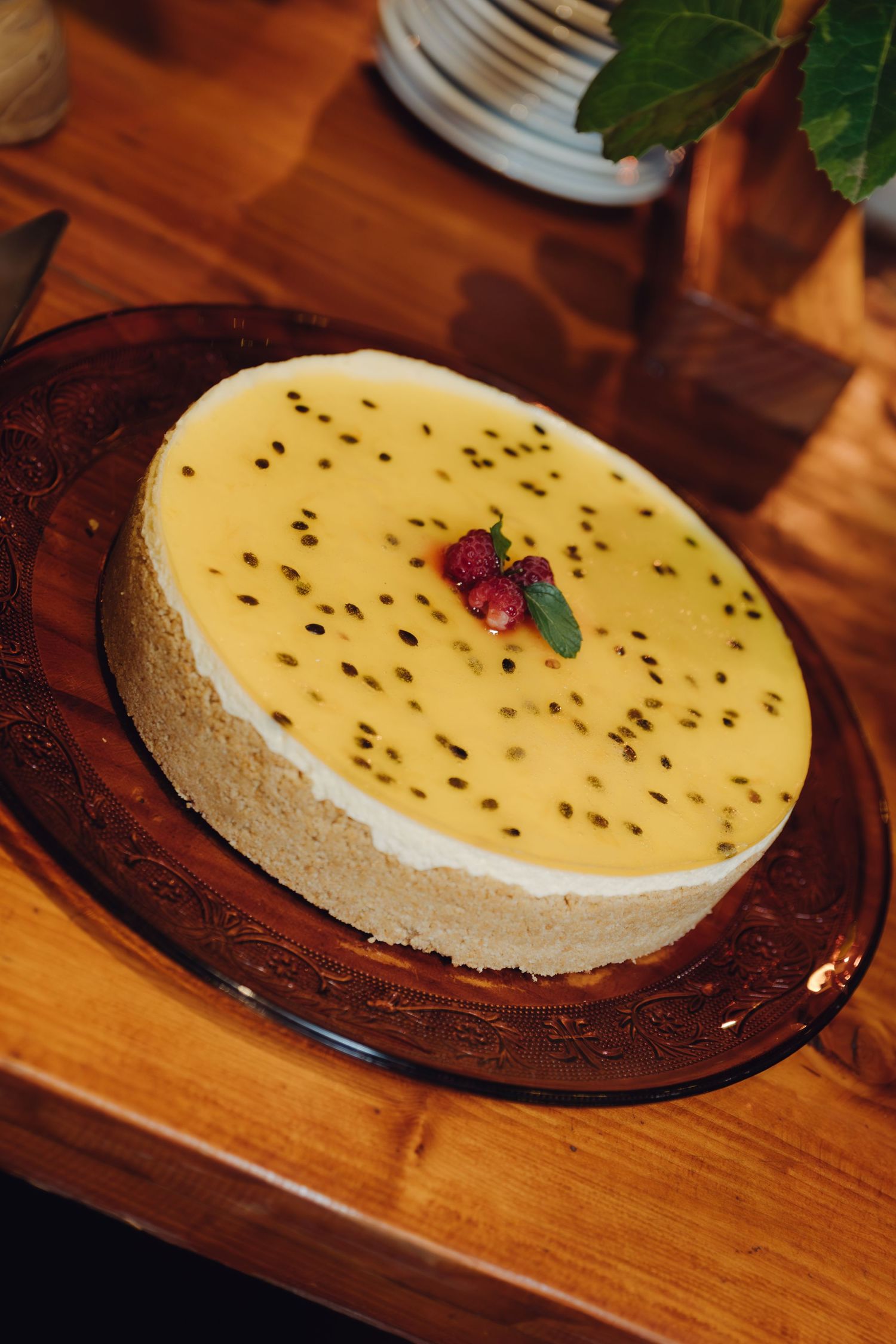 Passion fruit cheesecake topped with yellow glaze, seeds, and fresh berries on a decorative brown plate.