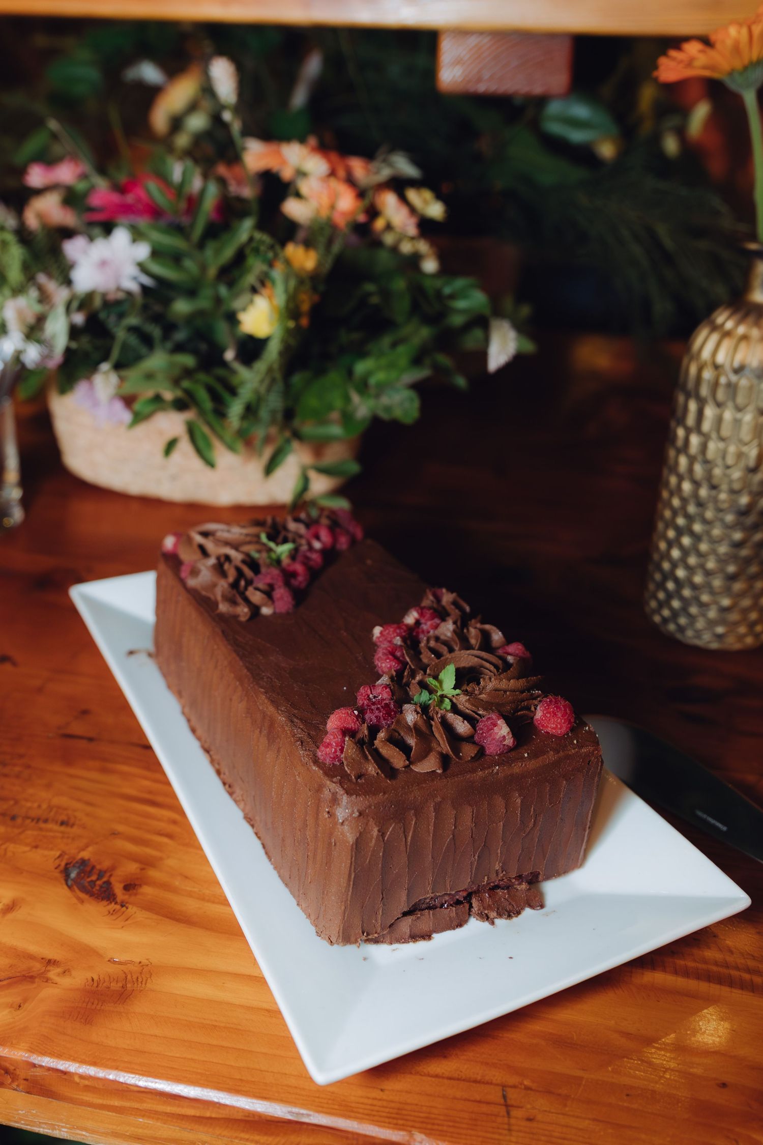 Elegant chocolate loaf cake decorated with raspberries and mint leaves on a white plate at a wedding.